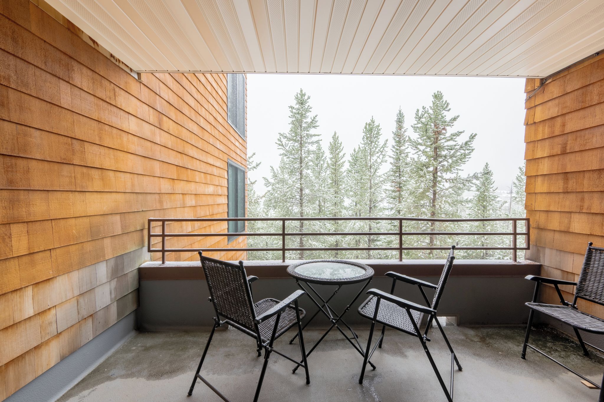 Un balcon avec une table et des chaises, des murs en bois et une vue sur les arbres.