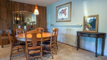 A dining area with a wooden table and chairs, a mirror, and two framed pictures on the wall.