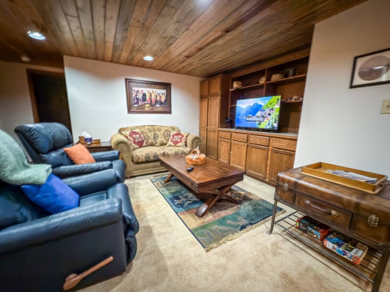 A living room with a leather sofa, a wooden coffee table, a patterned rug, a television, and wooden cabinets.