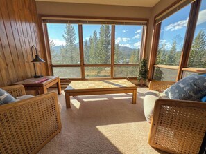 A cozy room with a large window, a wooden table, wicker furniture, and a view of trees and mountains. - 3BR Big Sky Condo Sleeps 9, Walk to Free Shuttle (Big Sky)