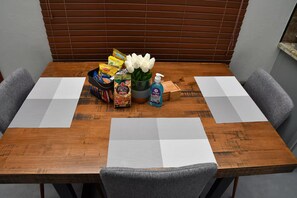A wooden dining table with placemats, a basket of snacks, a bottle of hand sanitizer, and a vase with white flowers. - Cozy apartment with AC close to good food, supermarket and local attractions (Kingston)