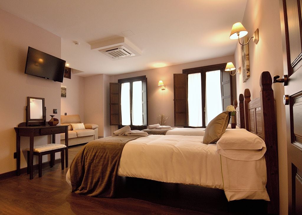 A hotel room with a bed, a desk, a chair, a television, and a window with shutters.