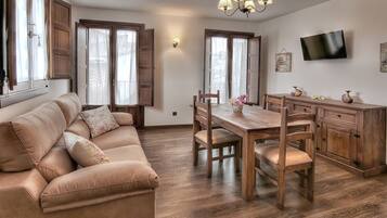 A modern living space with a sofa, dining table, chairs, wooden cabinets, a television, and large windows.