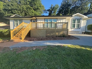 A residential house with a wooden staircase leading to a deck, surrounded by a well-maintained lawn. - Just Like New-Modern 3 Bedroom House Near HOTLANTA (Decatur)