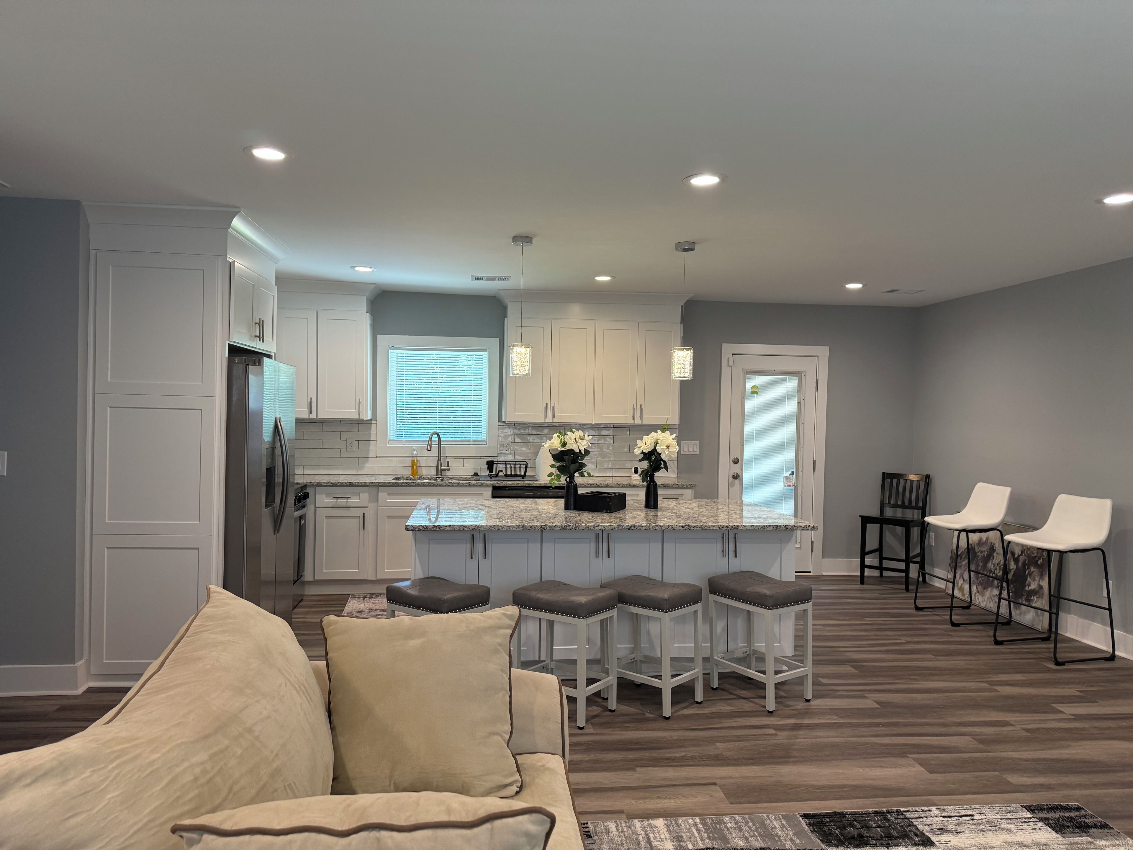 A modern kitchen with white cabinets, a central island with bar stools, and a dining area with chairs.