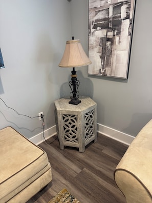 A corner of a room with a side table, a lamp, a power outlet, and a piece of abstract art on the wall. - Just Like New-Modern 3 Bedroom House Near HOTLANTA (Decatur)