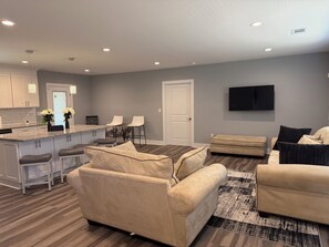 A modern living room with a beige sofa, a coffee table, and a TV mounted on the wall. - Just Like New-Modern 3 Bedroom House Near HOTLANTA (Decatur)