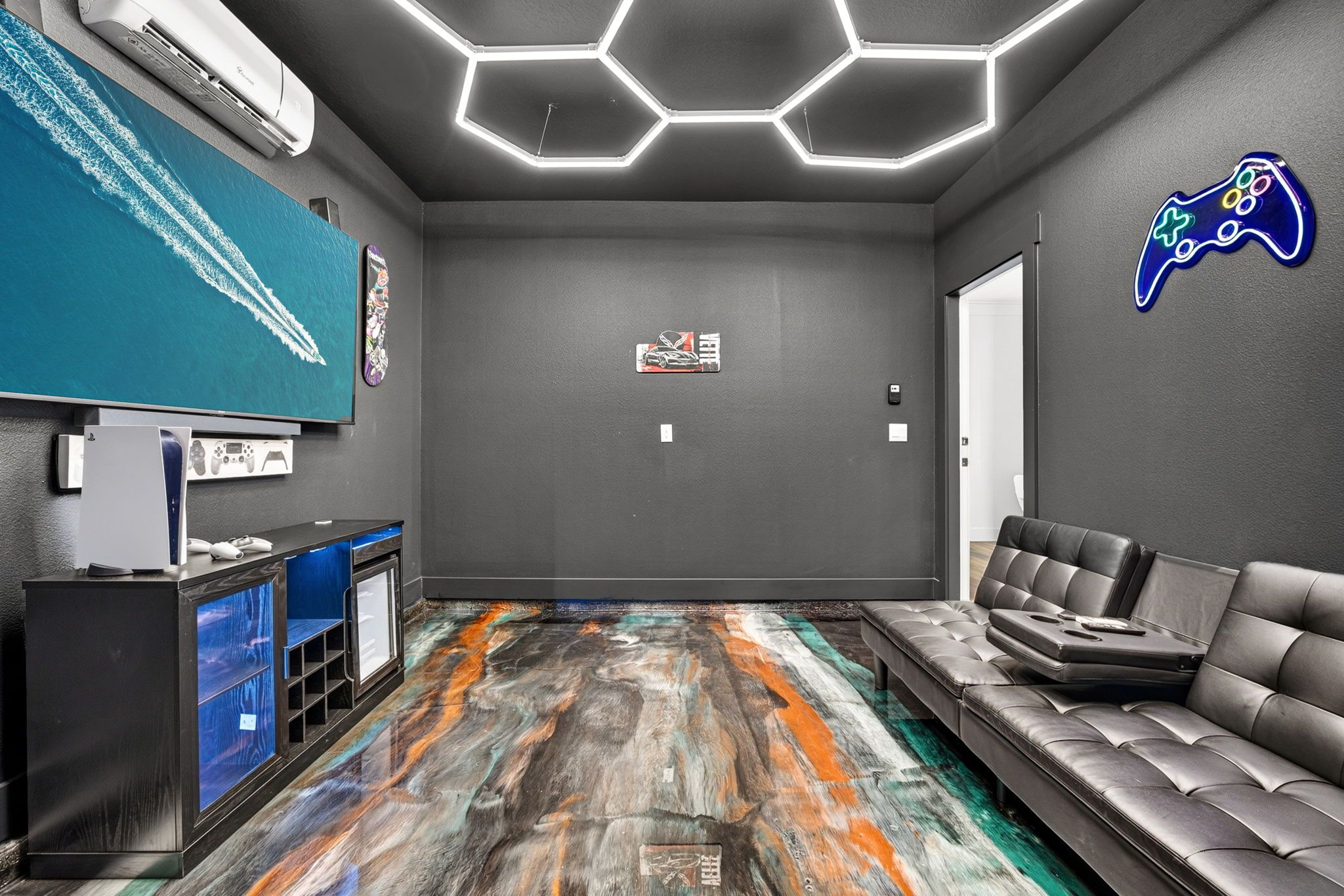 A modern gaming room with a large screen, gaming console, and comfortable seating.