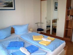Ein Hotelzimmer mit zwei Betten, einem Kleiderschrank, einem Stuhl und einem Bücherregal.