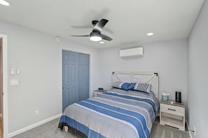 Ein Schlafzimmer mit Bett, Nachttischen, Deckenventilator, Klimaanlage und einer Tür.