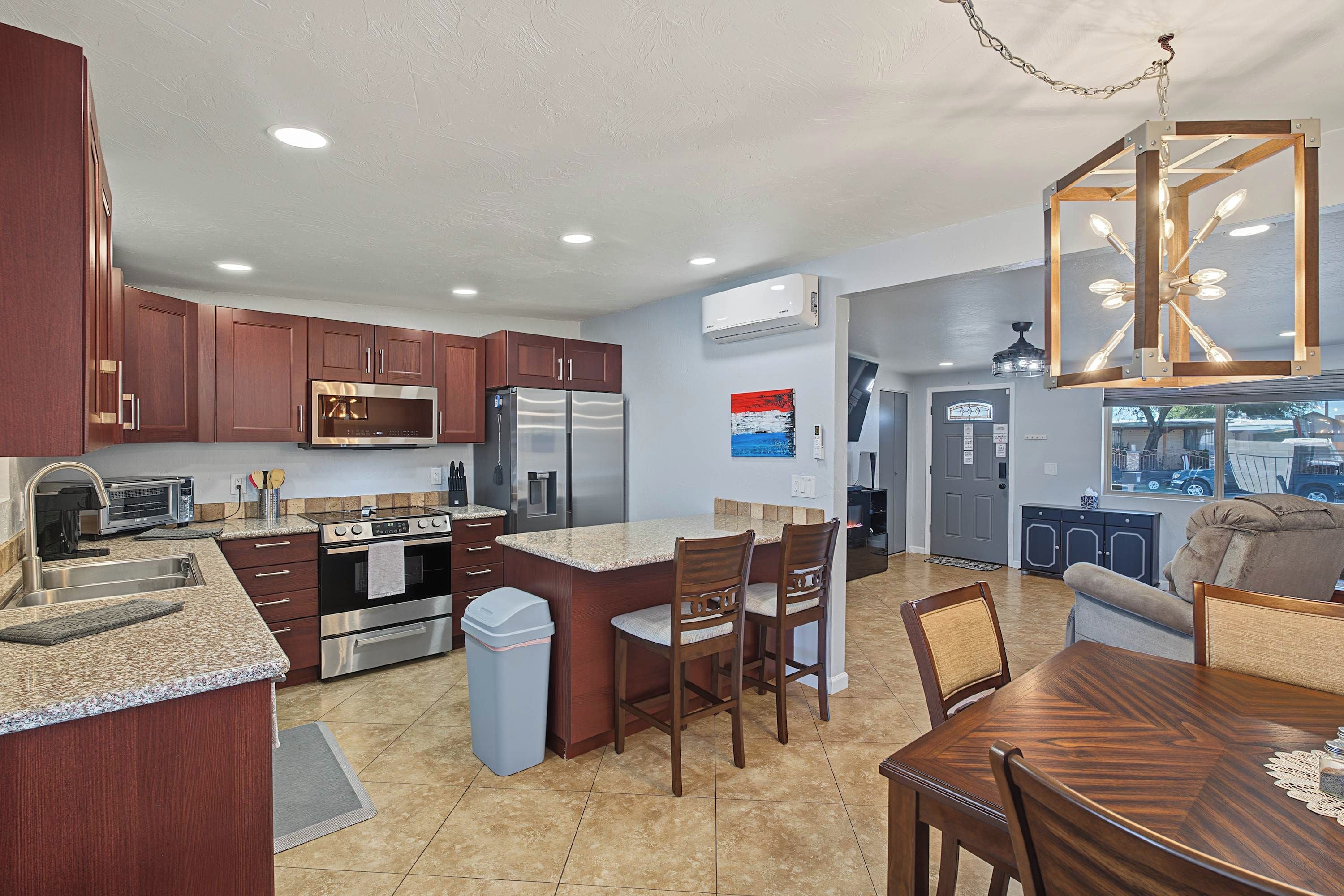 A modern kitchen with stainless steel appliances, a dining area with a wooden table and chairs, and a view of the outside through a window.