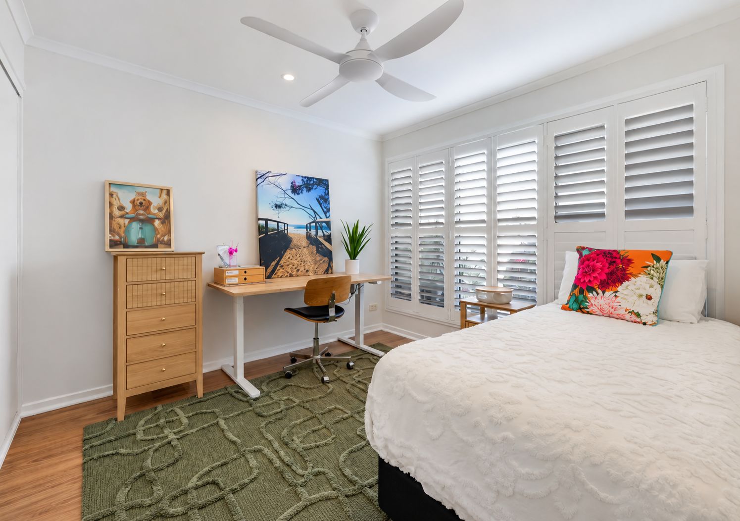 A bedroom with a bed, a desk, a chair, a dresser, a ceiling fan, and a window with blinds.