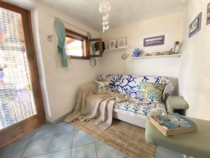 Ein Wohnzimmer mit einer Couch, einem Fenster mit Vorhängen, einer Deckenleuchte und einem Bücherregal.