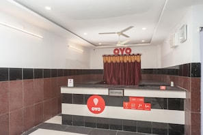 Un área de recepción con ventilador de techo, un letrero con la palabra 'OYO' y un anuncio de registro de entrada y salida con horario de atención.