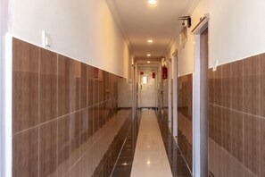 A corridor with tiled walls and a reflective floor, leading to a door with a fire extinguisher mounted on the wall. - Collection O Srinivasa Residency (Tirupati)