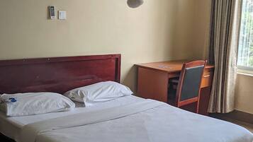 A hotel room with a bed, a desk, a chair, a bedside table, and a window with curtains.