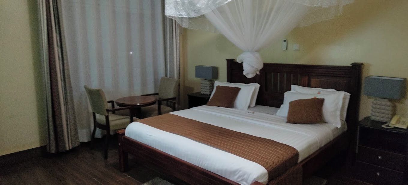 A hotel room with a bed, bedside tables, a chair, a small table, and a window with curtains.
