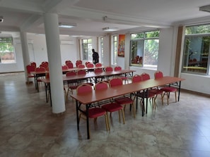 A spacious room with multiple tables and chairs, large windows, and a person standing in the background. - Pearl On The Nile Hotel Jinja (Jinja)