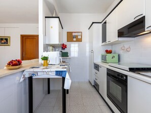 A compact kitchen with white cabinets, a microwave, a stove, and a small refrigerator. - Morosita Home by Interhome (Alghero)
