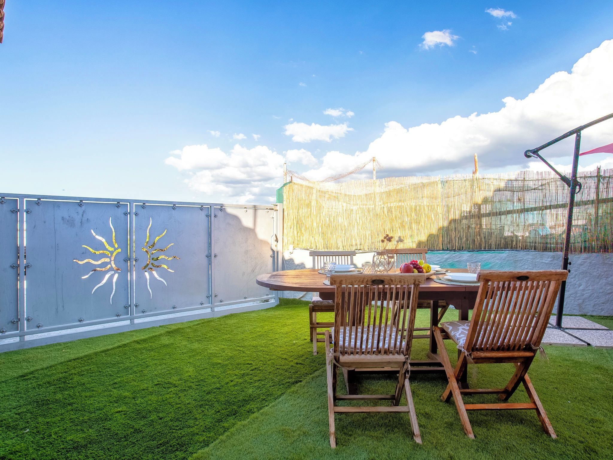A patio with a round table and chairs, a grassy lawn, and a view of the sea.