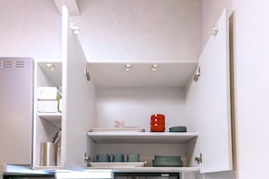 A kitchen with white cabinets, a refrigerator, and a shelf with plates and cups.