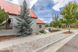 A residential area with a house featuring a red roof, a large evergreen tree, and a gravel driveway. - Sanctuary Stay: A Historic Converted Church in Downtown Salida (Salida)