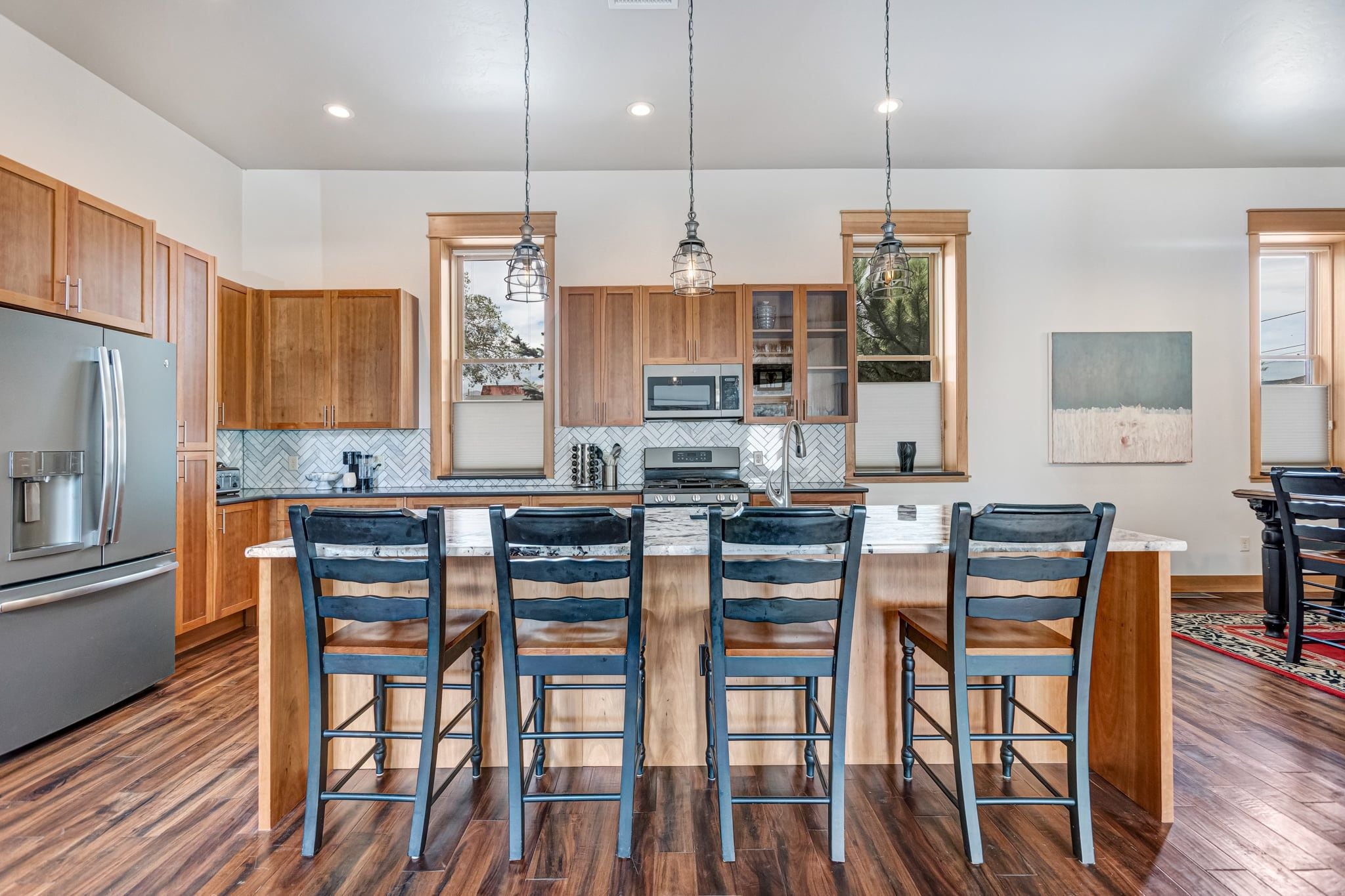 A modern kitchen with wooden cabinets, a stainless steel refrigerator, a built-in oven, and a central island with bar stools.