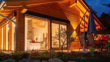 A modern wooden house with a glass door entrance leading to a kitchen and living area.