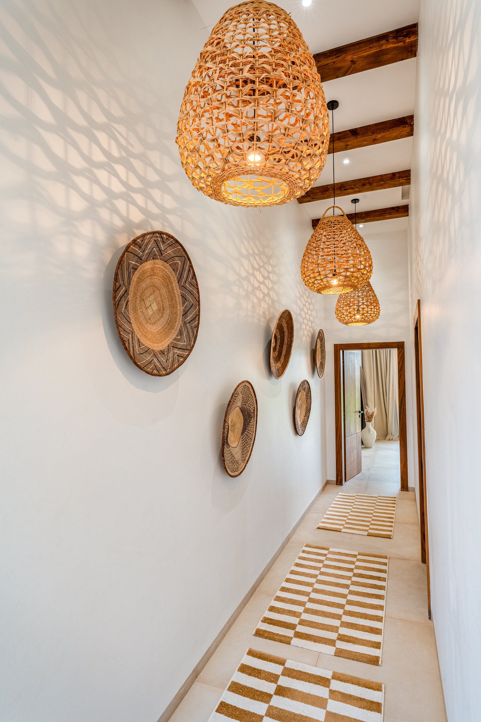 Un couloir agrémenté de luminaires tressés, de décorations murales à motifs et d’un tapis à carreaux.
