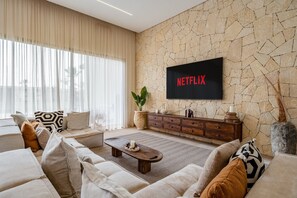 Un saló amb una paret de pedra, un televisor de pantalla plana muntat sobre una consola de fusta, i una finestra gran amb cortines primes.