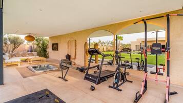 A covered outdoor gym area with exercise equipment, a hot tub, and a seating area with a sofa and table.