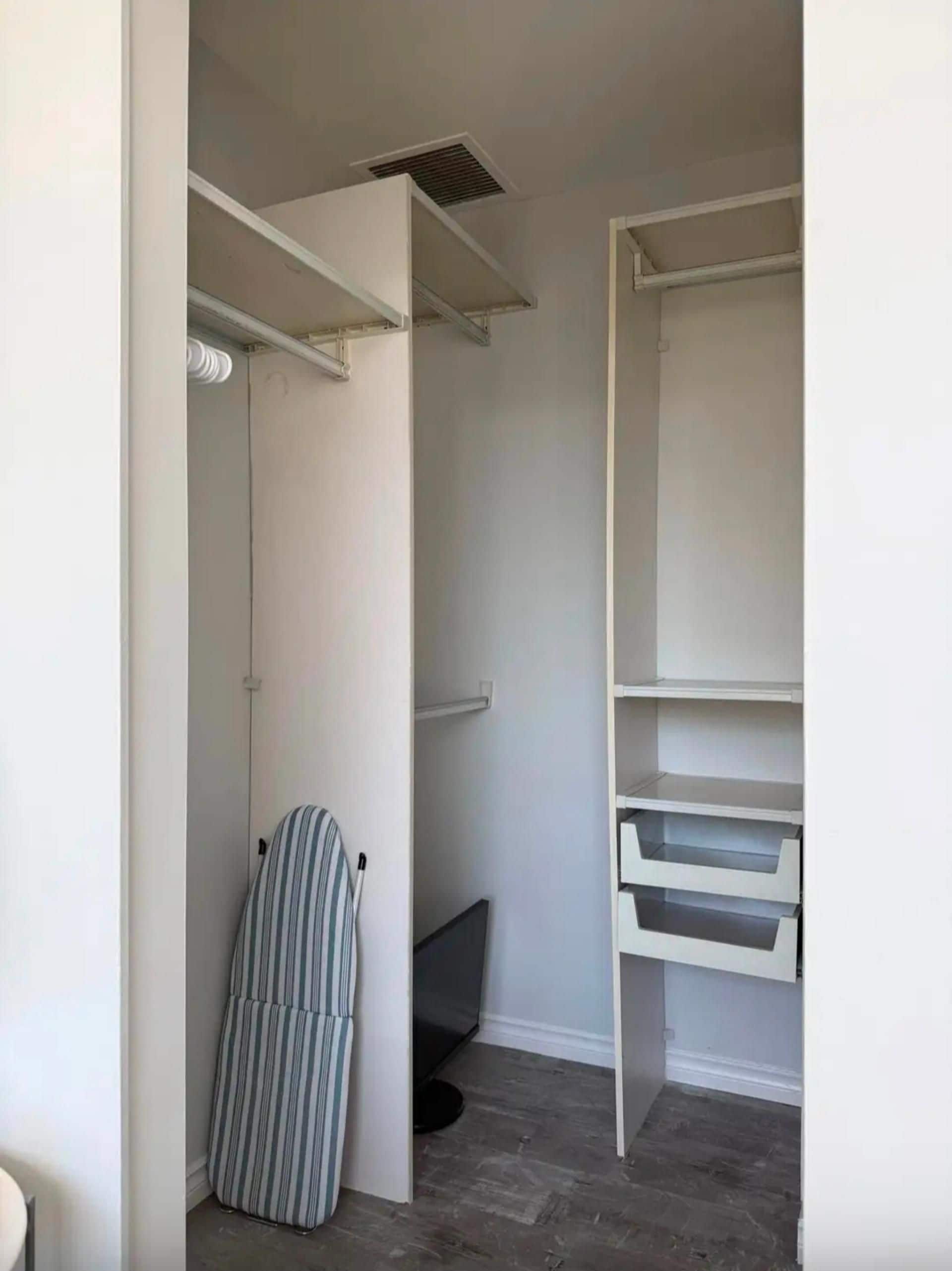 Un dressing sans porte avec des étagères ouvertes, une tringle à vêtements et une chaise à rayures.
