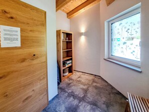 A narrow hallway with a wooden door, a wooden shelf unit, a window with a floral pattern, and a light fixture. - Adlerhorst by Interhome (Auffach)