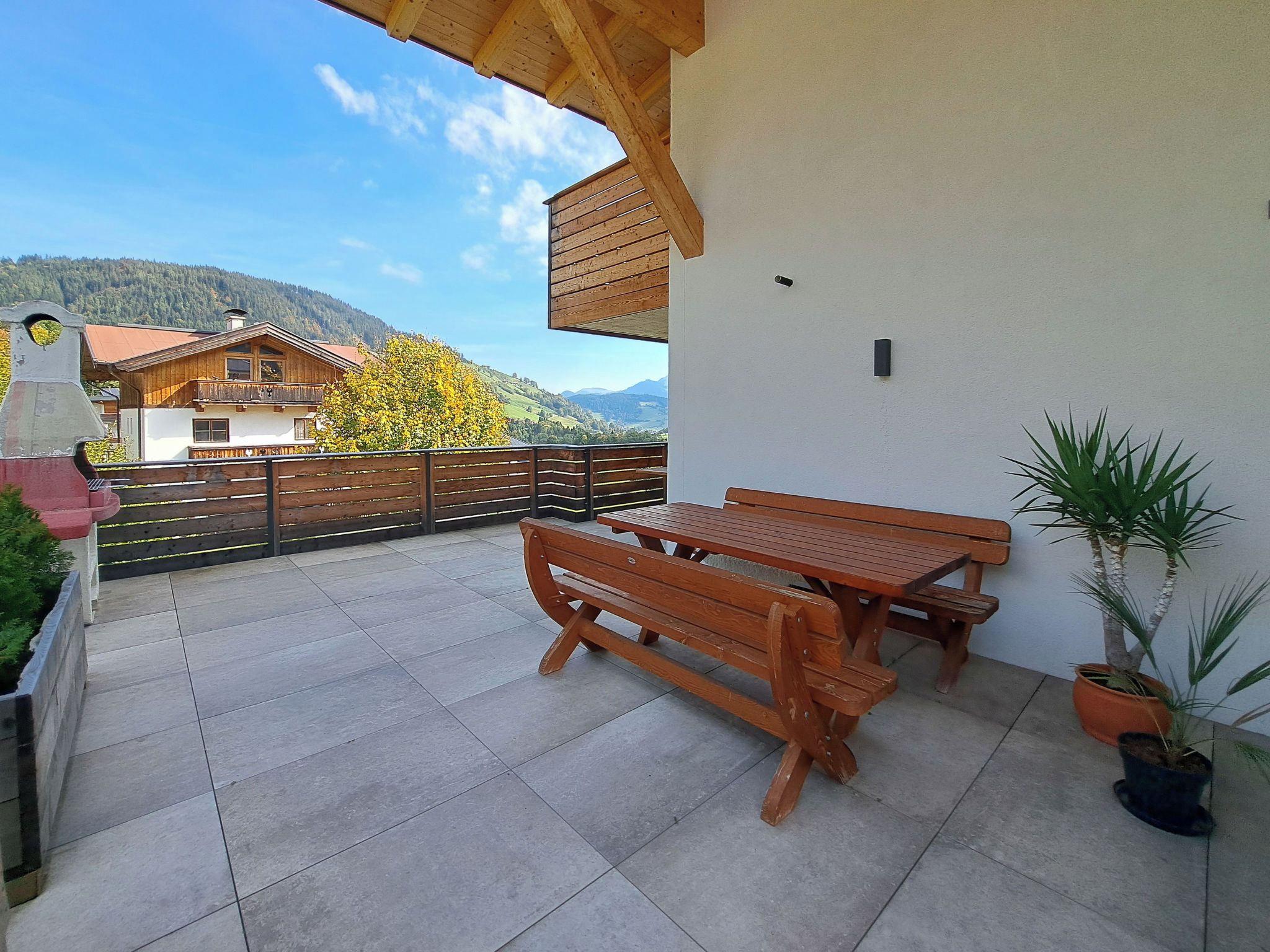 A wooden bench and table set on a balcony with a view of a mountain and a house.