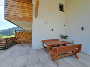 A wooden outdoor seating area with a table and benches, a stack of firewood, and a view of a mountainous landscape. - Bärenhöhle by Interhome (Auffach)