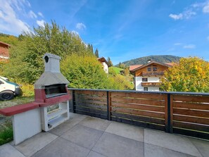 A patio with a barbecue grill, a wooden fence, and houses in the background. - Bienenwiese by Interhome (Auffach)