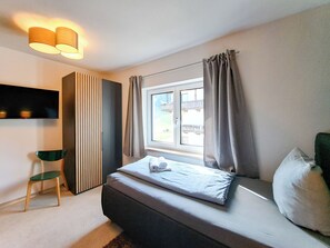 Een moderne slaapkamer met een bed, een televisie, een stoel en een raam met gordijnen.