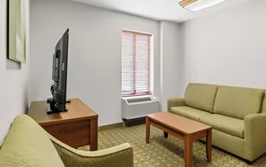 Ein Wohnzimmer mit einer Couch, einem Couchtisch, einem Fernseher auf einem Schrank und einem Fenster mit Jalousien.
