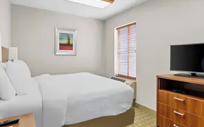 Ein Hotelzimmer mit Bett, Fernseher, Schreibtisch und einem Fenster mit Jalousien.