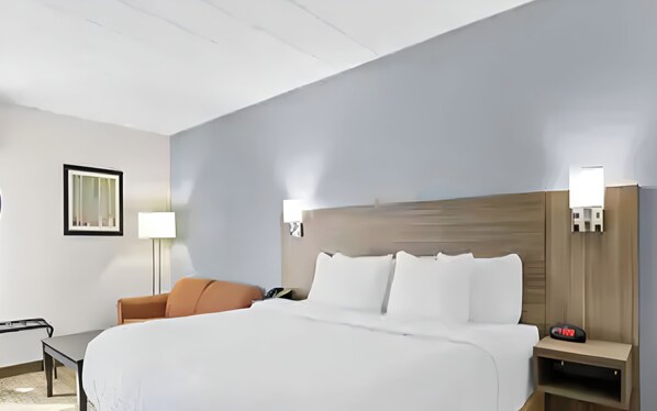 Habitació d'hotel amb un llit, escriptori, cadira i tauleta de nit amb un rellotge.