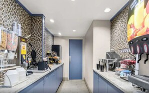 Una cuina professional amb una porta blava, una màquina de cafè i un dispensador de suc de fruita.