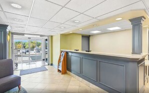 Una zona de recepció amb mostrador, un espai d'espera amb una cadira i vista a través de les portes de vidre.