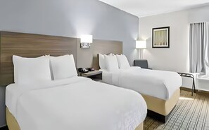 Ein Hotelzimmer mit zwei Betten, einem Schreibtisch, einem Stuhl, einer Lampe und einem Fenster mit Vorhängen.