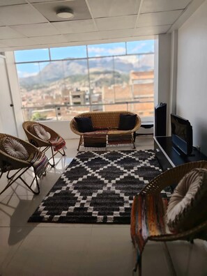 A balcony with wicker furniture, a black and white patterned rug, and a television.