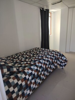 A room with a bed, a window with curtains, and a tiled floor.