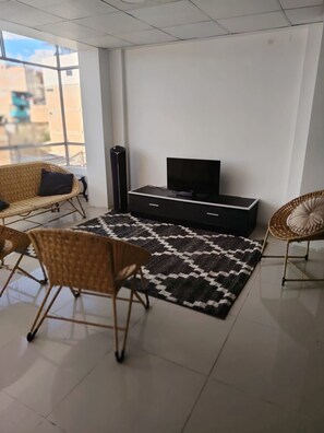 A modern living room with a flat-screen TV, two wicker chairs, a black entertainment unit, and a patterned rug.