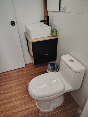 A bathroom with a white toilet, a wooden vanity with a white sink, and a black cabinet.