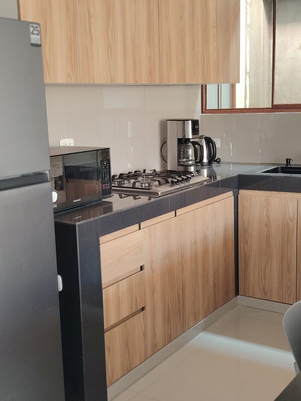 A modern kitchen with wooden cabinets, a gas stove, a microwave, and a coffee maker.