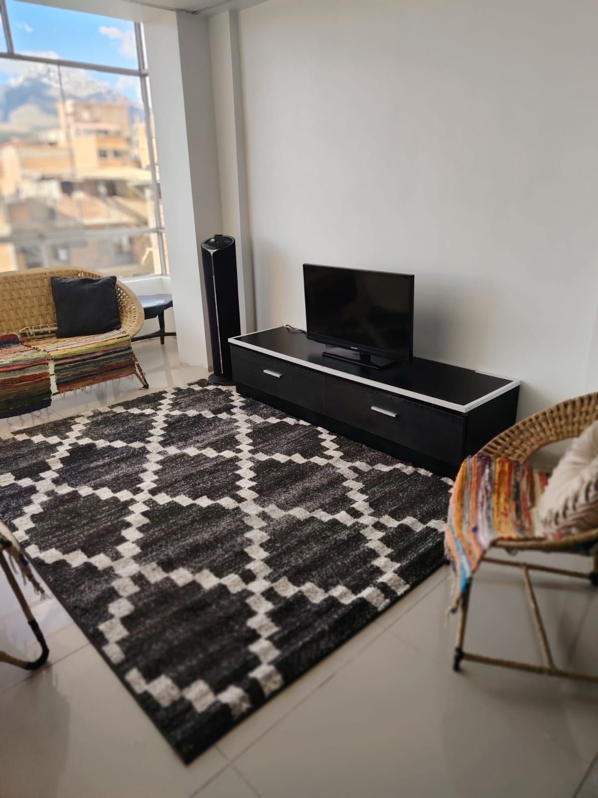 Ein modernes Wohnzimmer mit einer schwarzen Unterhaltungseinheit, einem gemusterten Teppich und Korbmöbeln.
