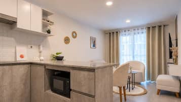 Una cocina moderna con electrodomésticos integrados, un comedor con una silla y una mesa, y un ventanal con cortinas.